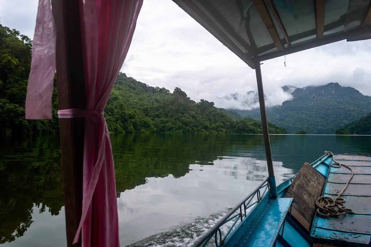 Uitzicht vanaf een houten motorboot over het stille meer met beboste bergen en laaghangende wolken