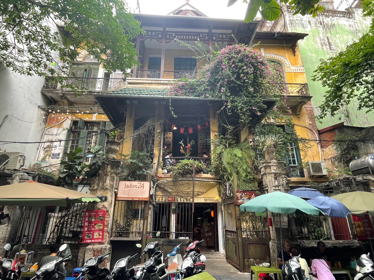 De gele koloniale villa van koffiezaak Loading T in Chân Cầm, met bloeiende bougainville en geparkeerde scooters