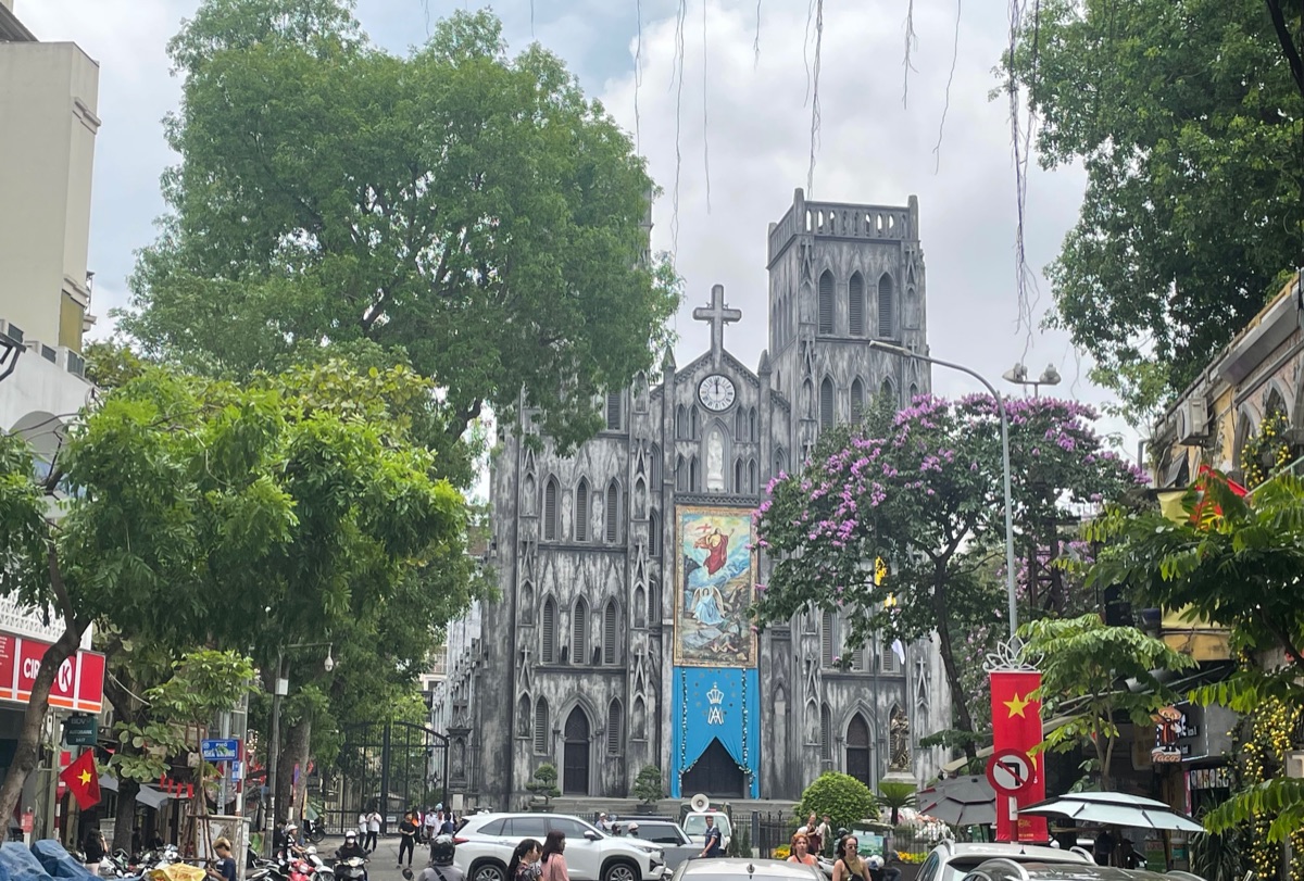 De grijze neogotische gevel van de Sint-Jozefkathedraal in Hanoi, tussen bloeiende bomen