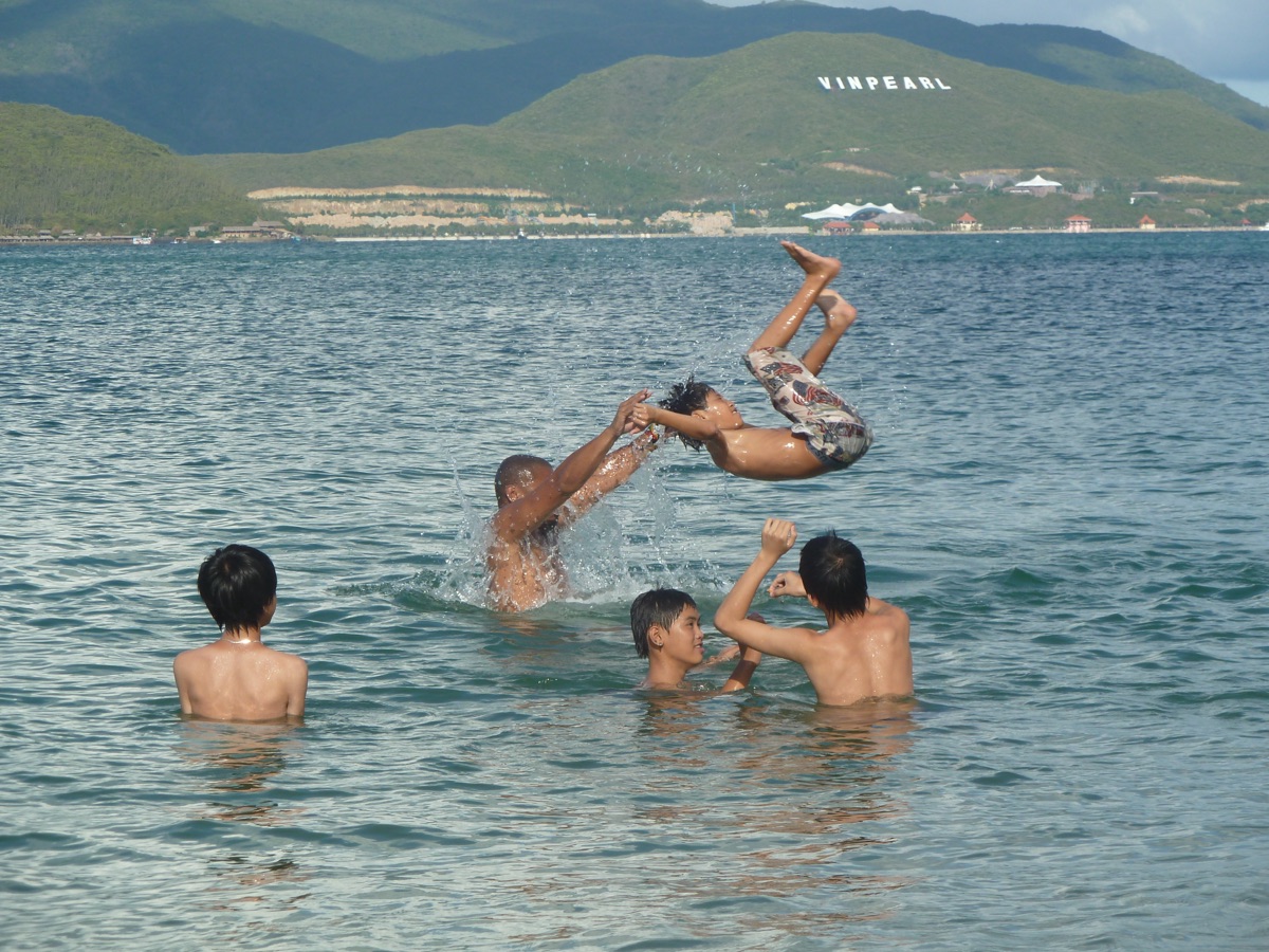 Jongens spelen in het kalme water van de baai, met het groene eiland Hon Tre op de achtergrond