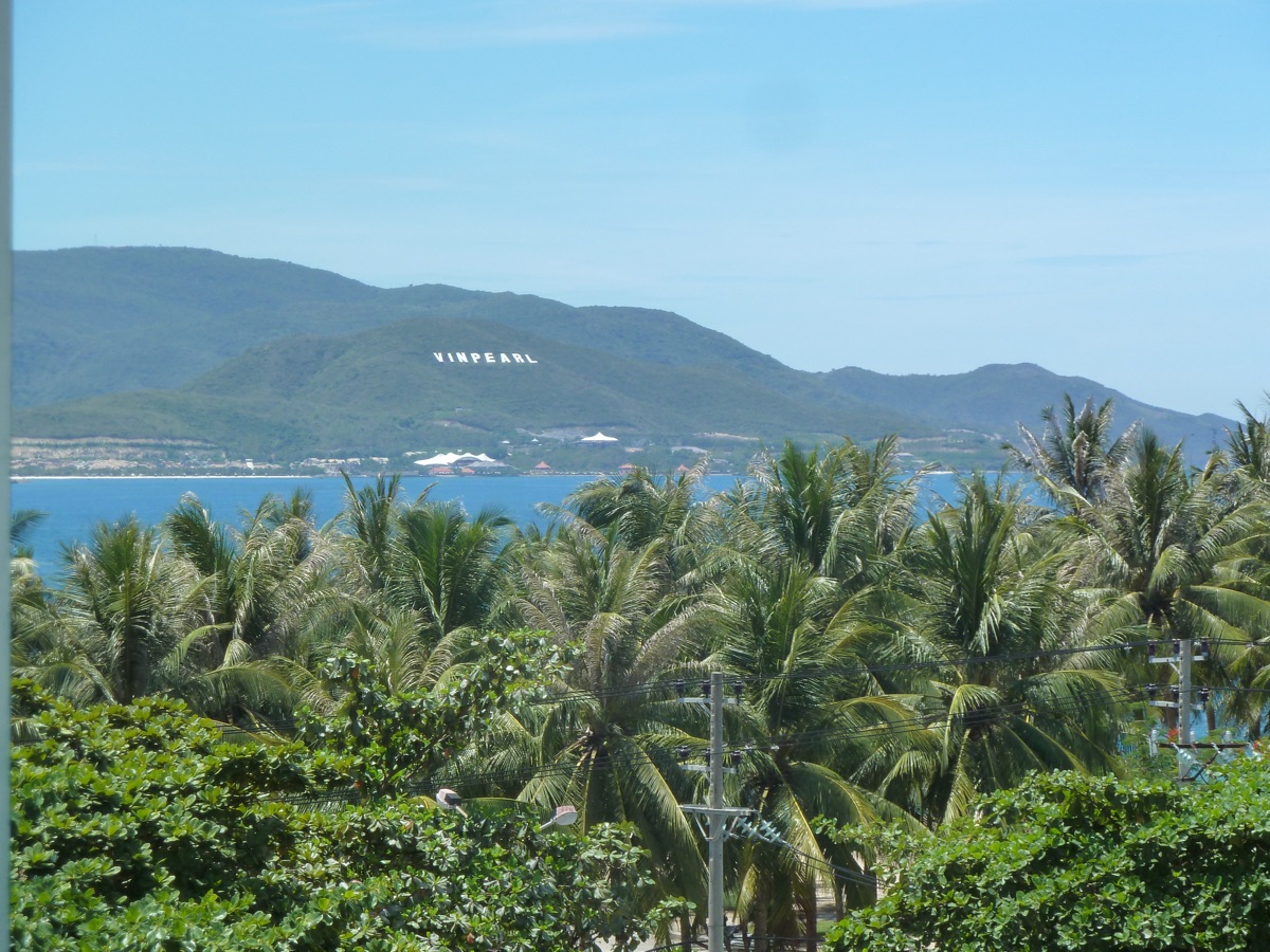 Uitzicht over palmbomen en de baai naar het eiland Hon Tre, met de letters van Vinpearl op de heuvel