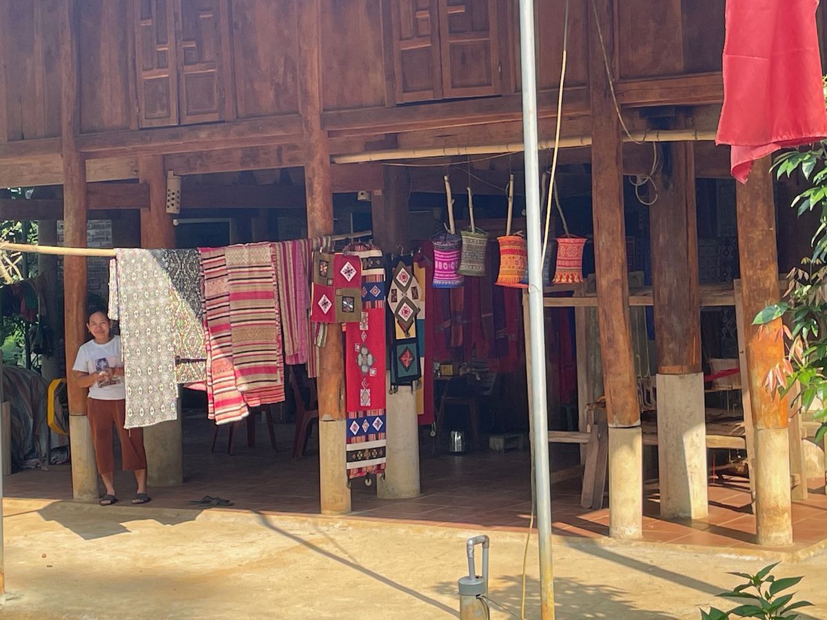 Kleurrijk geweven textiel te koop onder een houten paalwoning in Pu Luong
